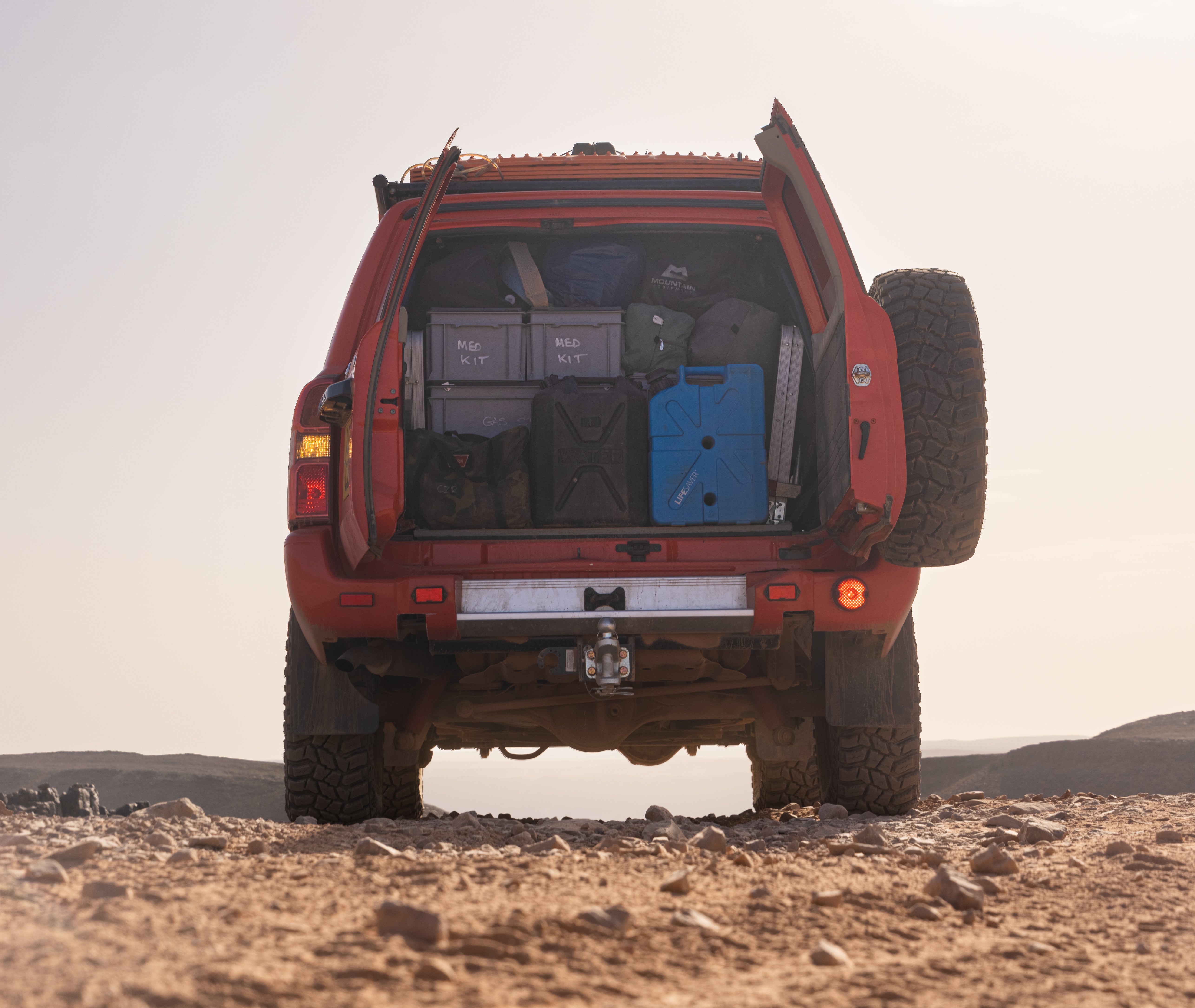 Red off-road vehicle with open doors and a LifeSaver Jerrycan in a desert setting